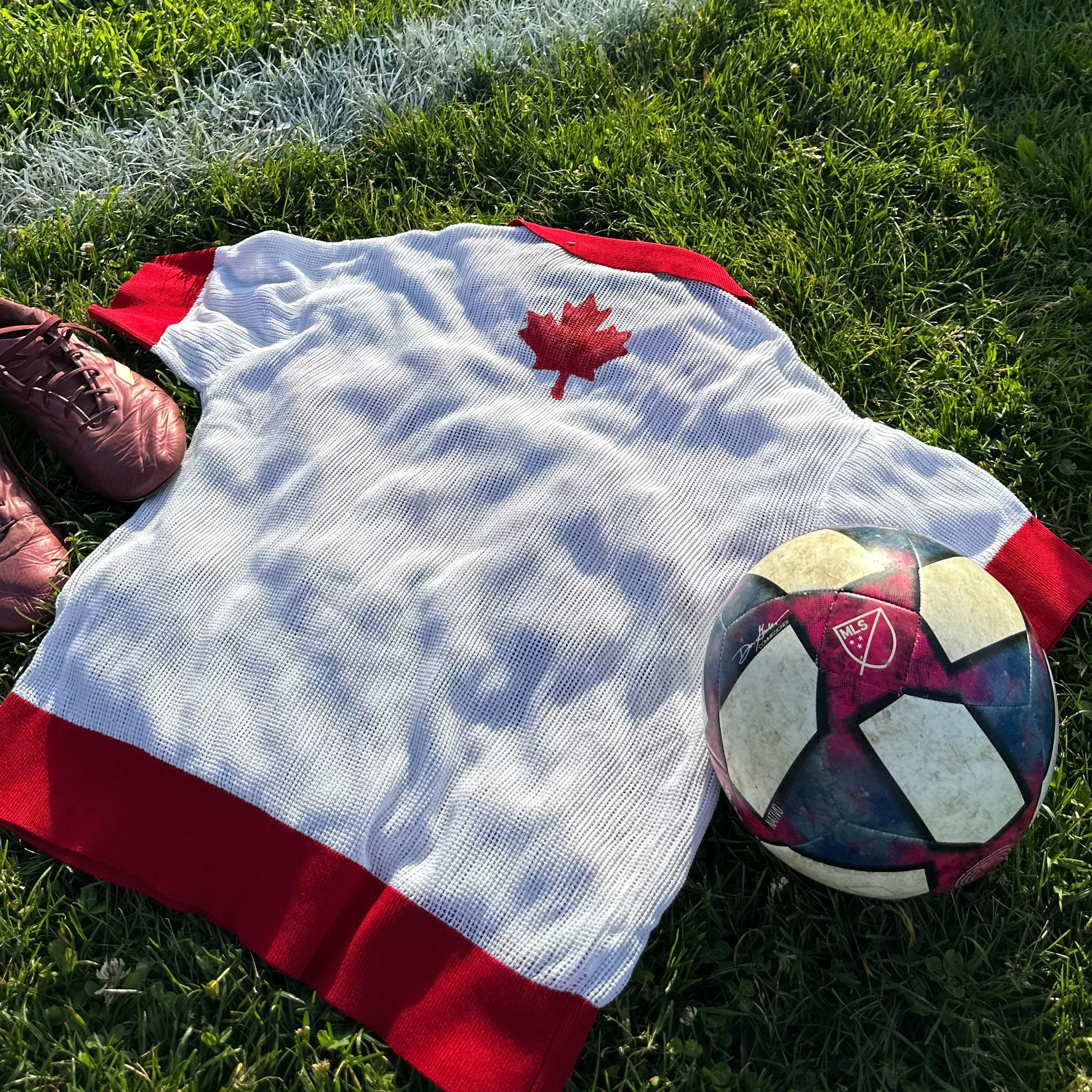 Sweater with a maple leaf and soccer ball on grass